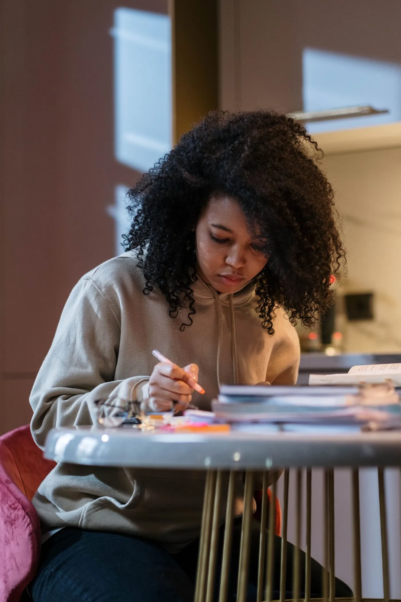 A student writes notes at a small table with a stack of books beside her.